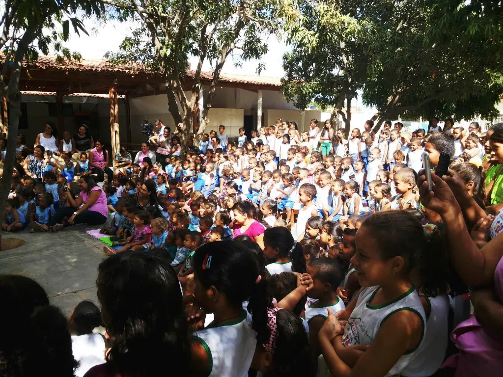 Crianças e educadores reunidos em pátio escolar durante uma apresentação ou atividade coletiva.