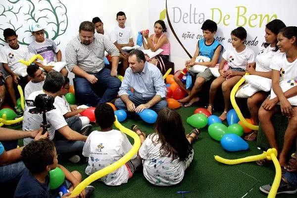 Jovens sentados em roda participam de dinâmica com balões, com banner “Delta De Bem” ao fundo.